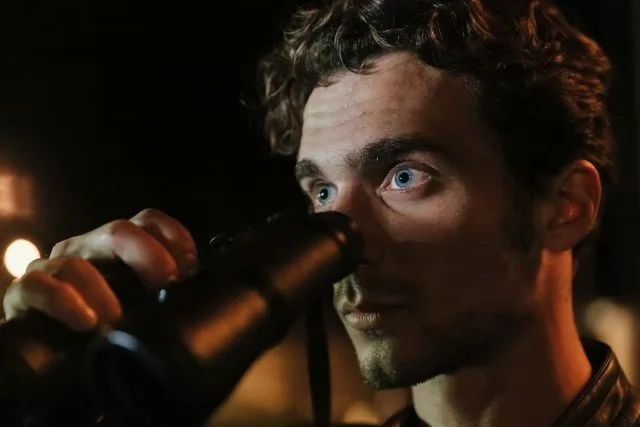 Close-up of a man with intense gaze using binoculars during night time observation.