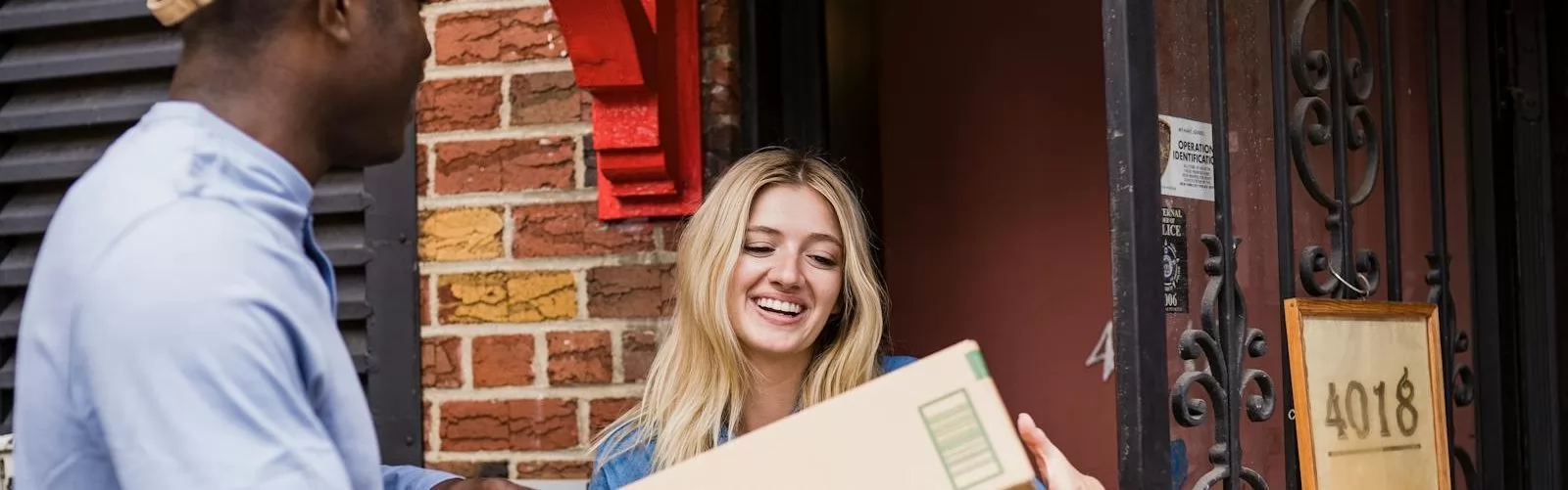 A cheerful woman receives a package from a courier at her door, showcasing friendly delivery service.