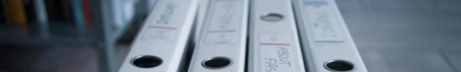 Four labeled office binders organized neatly on a wooden shelf in an indoor setting.