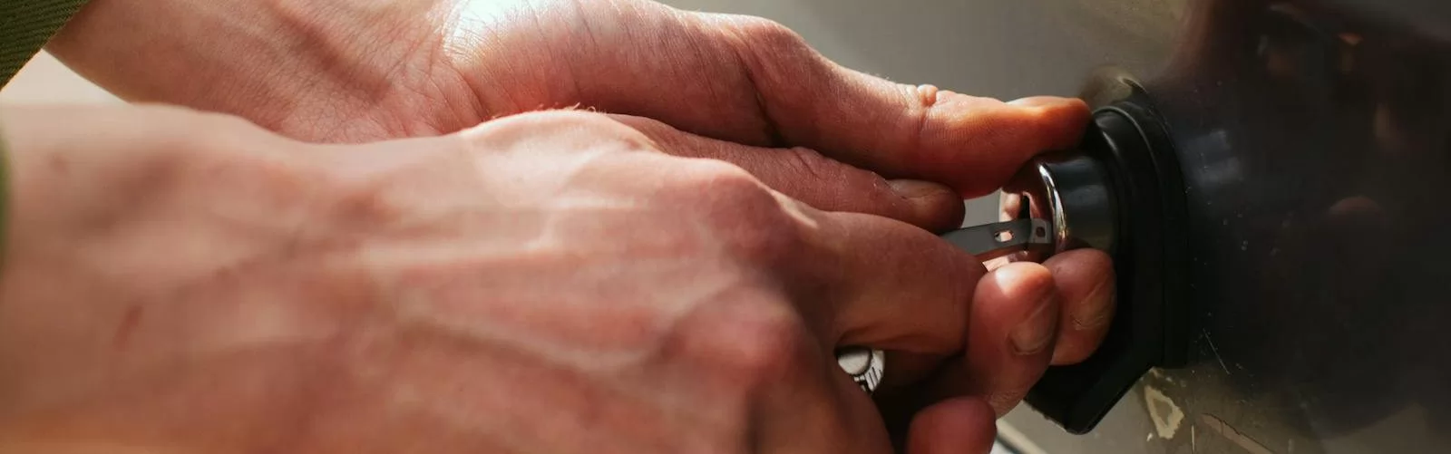 Close-up of hands unlocking a vehicle trunk with a key, showing detail and reflection.